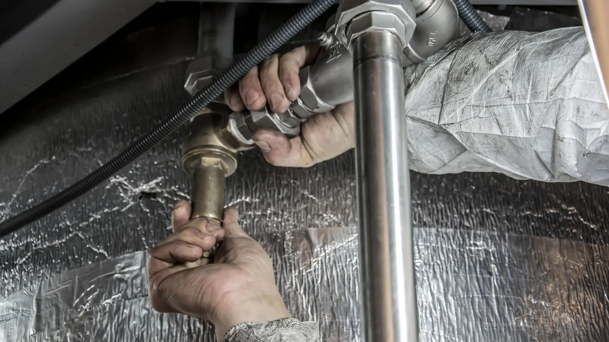 A plumber working on pipes under a sink